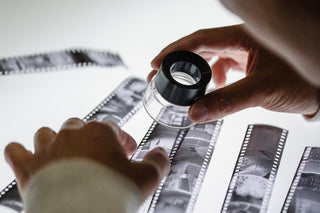 A technician examines strips of film negatives on a light table with a loupe.