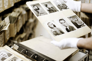 A technician wearing white gloves holds a page from an album with old photographs on it