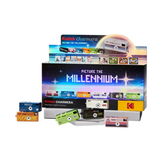 A retail display box and several retro-style Kodak Charmera film cameras arranged in front on a plain white background. The display features colorful cameras and a large back panel reading 'Picture the Millennium' with Kodak branding.