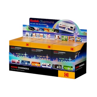 A retail display box of Kodak Charmera Keychain Digital Cameras, featuring three individual cameras mounted on a colorful cardboard stand with vintage-style camera illustrations and Kodak branding.