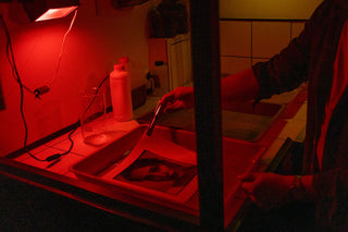 In the darkroom with a red light, a technician works with sensitive print development