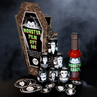 A Halloween-themed monster movie gift set from Film Photography Project featuring a large coffin-shaped Monster Film Gift Box, a bottle of Monster Sauce hot sauce, several black metal cans with character labels, and multiple round character coins, all arranged on a dark smoky background.