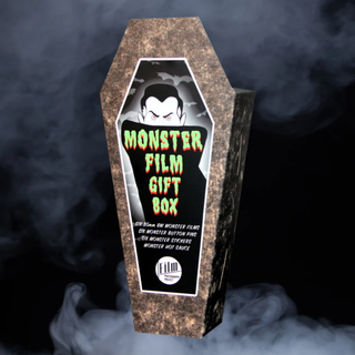 A coffin-shaped Monster Film Gift Box from Film Photography Project with a textured brown stone-like exterior and a black front label featuring a vampire illustration and green text, shown against a smoky dark background.