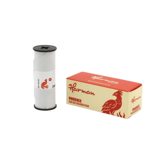 A spool of Harman Phoenix color film next to its cream and red cardboard packaging box, shown on a plain white background.