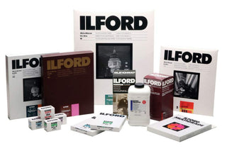 An arrangement of Ilford film products including sheet film in various sizes, rolls of film in boxes and an assortment of Ilford brand chemicals.