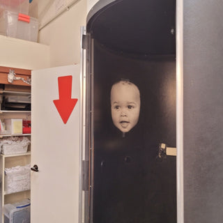 The darkroom at Photolab Berkeley, with a baby face print taped to the sliding entryway and a big red arrow directing foot traffic